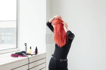 Téléchargez les photos : "Belle fille rousse aux cheveux longs, elle tisse une tresse, dans un salon de beauté. Soins capillaires professionnels et création de coiffures
." - en image libre de droit