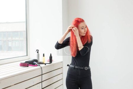 Photo for "Beautiful red-haired girl with long hair, she is weaves a braid, in a beauty salon. Professional hair care and creating hairstyles." - Royalty Free Image