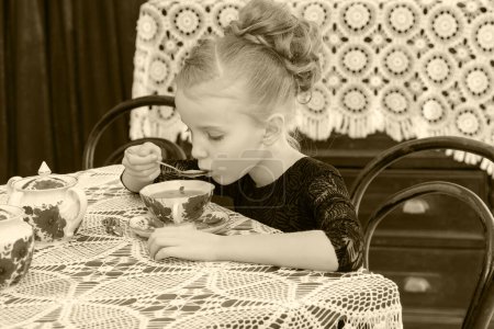 Téléchargez les photos : "Belle petite fille buvant du thé à la table
." - en image libre de droit