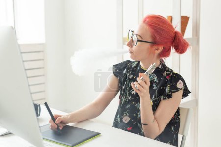 Photo for Female graphic designer working on computer while using graphic tablet at desk in the office and smoking a vape - Royalty Free Image