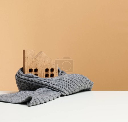 Foto de Casa en miniatura de madera envuelta en una bufanda de punto gris. Concepto de aislamiento de edificios, préstamos para reparaciones - Imagen libre de derechos