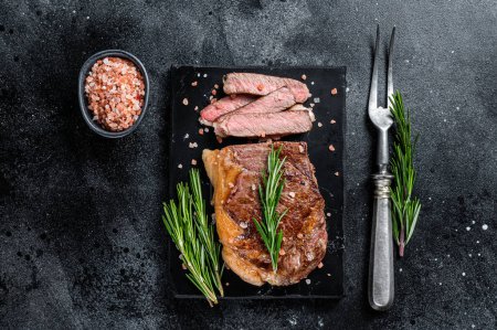 Photo for "Cut roasted new york strip beef meat steak or striploin on a marble board. Black background. Top view" - Royalty Free Image