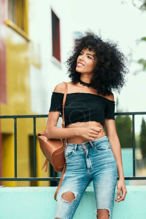 Foto de "Sonriente mujer mixta con pelo afro de pie en la calle
" - Imagen libre de derechos