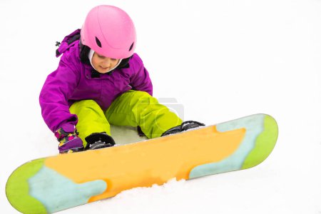 Photo for "Snowboard Winter Sport. little girl learning to snowboard, wearing warm winter clothes. Winter background." - Royalty Free Image