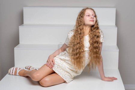 Téléchargez les photos : "Belle petite fille est assise sur l'escalier blanc." - en image libre de droit