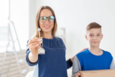 Téléchargez les photos : Belle maman floue et son fils tiennent les clés d'un nouvel appartement après la crémaillère. Nouveau concept et options hypothécaires pour une jeune famille. Famille monoparentale - en image libre de droit