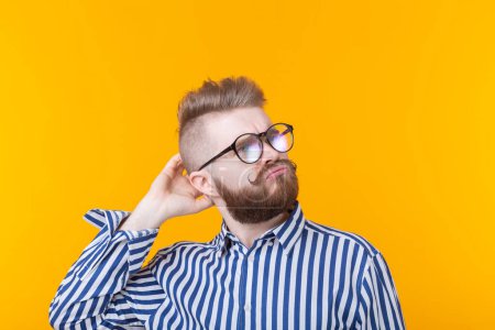 Photo for Cute intelligent young man with a beard and with glasses poses on a yellow background and thinks about something. The concept of a difficult choice. - Royalty Free Image
