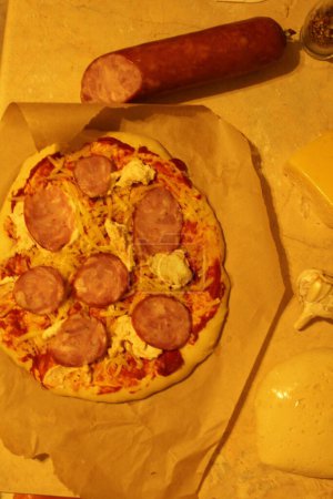 Foto de Pizza con salchicha de jamón. Comidas caseras de pizza se encuentran en el pergamino junto a la salchicha. Vista superior - Imagen libre de derechos