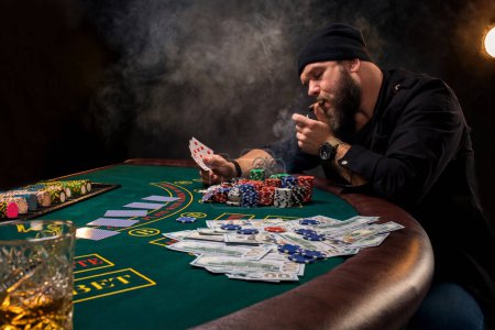 Foto de "El hombre está jugando al póquer con un cigarro y un whisky. Un hombre ganando todas las fichas en la mesa con humo de cigarrillo grueso
." - Imagen libre de derechos