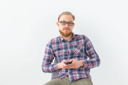 Téléchargez les photos : Barbu bel homme en chemise à carreaux avec téléphone portable sur fond blanc - en image libre de droit