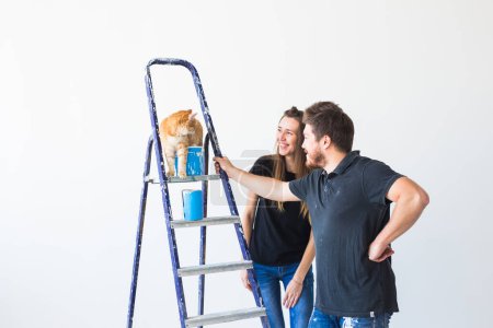 Foto de Reparación, renovación, concepto de pareja de mascotas y amor - familia joven con gato haciendo reparación y pintando paredes juntas y riendo - Imagen libre de derechos