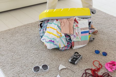 Foto de Concepto vacaciones, viajes y vacaciones - Mujer tratando de cerrar la maleta con un montón de cosas - Imagen libre de derechos