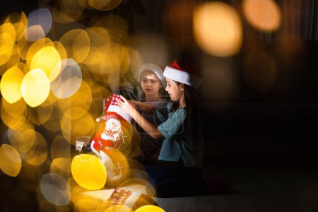 Téléchargez les photos : Petits enfants ouvrant des cadeaux à côté de la cheminée dans une maison confortable célébrant Noël - en image libre de droit