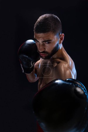 Photo for Man is hitting an opponent. Focused fighter with naked torso and boxing gloves looking at the camera. - Royalty Free Image