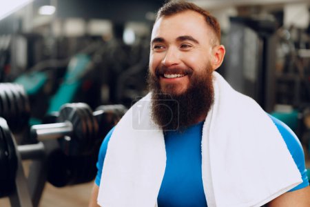 Téléchargez les photos : "bodybuilder jeune homme barbu en t-shirt bleu debout dans la salle de gym" - en image libre de droit