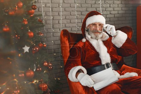 Téléchargez les photos : Homme en costume de Père Noël assis sur une chaise - en image libre de droit