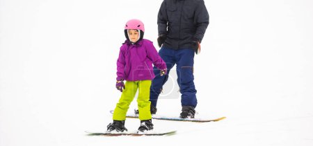 Photo for At Cold Winder Day at Mountain Ski Resort Father Teaching Little Daughter Snowboarding - Royalty Free Image
