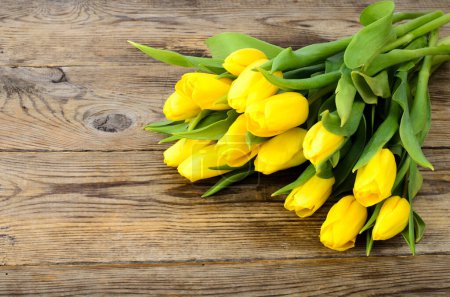 Photo for Yellow tulips lie on an old wooden surface - Royalty Free Image