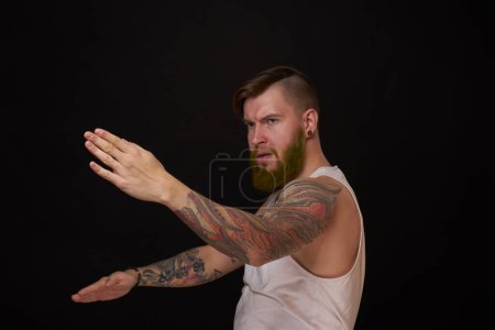 Photo for "bearded man with tattoos on his arms gesturing with his hands dark background" - Royalty Free Image