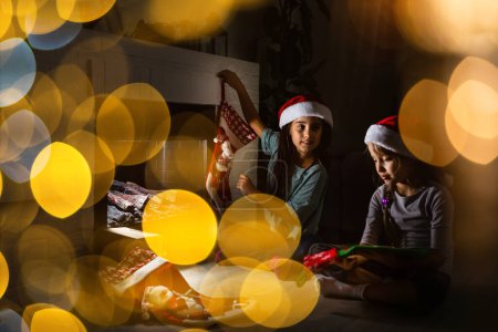 Photo for "Little kids opening presents next to the fireplace in a cozy home celebrating Christmas" - Royalty Free Image