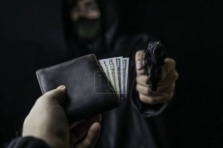 Foto de La mano del hombre extiende el bolso de dinero al ladrón con pistola. - Imagen libre de derechos