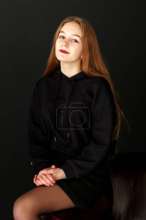 Photo for A teenage girl is sitting on a leather chair. - Royalty Free Image