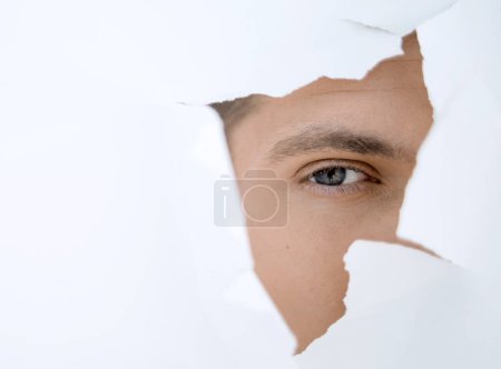 Téléchargez les photos : Jeune homme d'affaires regardant à travers un trou dans le mur de papier - en image libre de droit