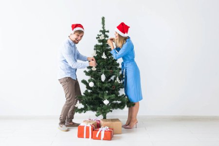 Foto de Vacaciones y concepto festivo - Pareja joven de la familia en sombreros de santa decoración del árbol de Navidad - Imagen libre de derechos