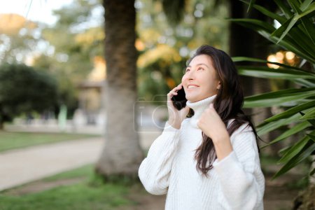 Foto de Chica china en el parque tropical hablando por teléfono inteligente cerca de la palma. - Imagen libre de derechos