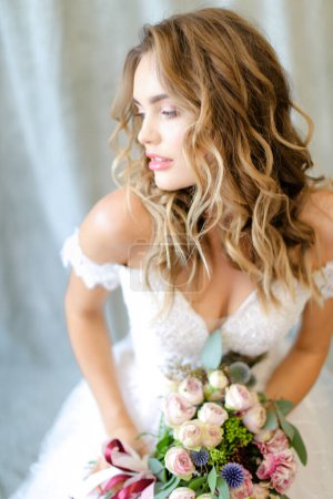 Téléchargez les photos : Jeune belle mariée portant une robe blanche avec bouquet au studio photo. - en image libre de droit