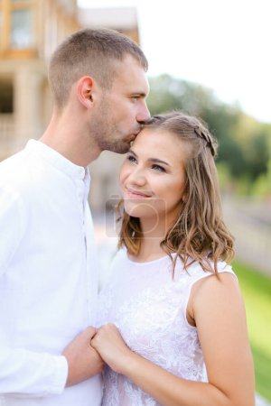 Photo for "Caucasian groom kissing bride and holding hands outside." - Royalty Free Image