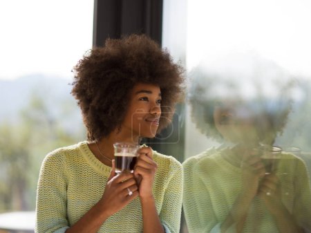 Foto de "Mujer afroamericana bebiendo café mirando por la ventana
" - Imagen libre de derechos