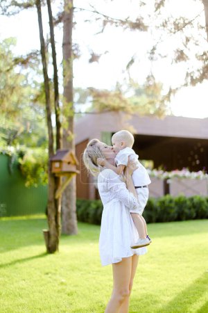 Téléchargez les photos : "Jeune mère blonde marchant avec bébé sur l'herbe dans la cour." - en image libre de droit