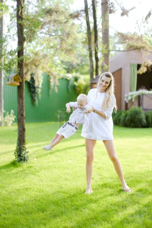 Photo for "Young european mother walking with babe on grass in yard." - Royalty Free Image