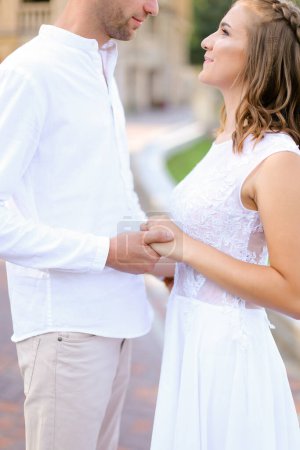 Téléchargez les photos : "Heureuse mariée caucasienne et marié tenant la main et debout à l'extérieur." - en image libre de droit
