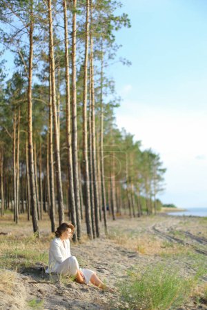Photo for Young lady sitting on sand beach with trees in background. - Royalty Free Image
