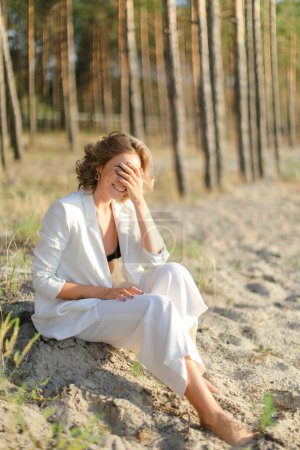 Téléchargez les photos : Young pretty woman sitting on sand beach with trees in background. - en image libre de droit
