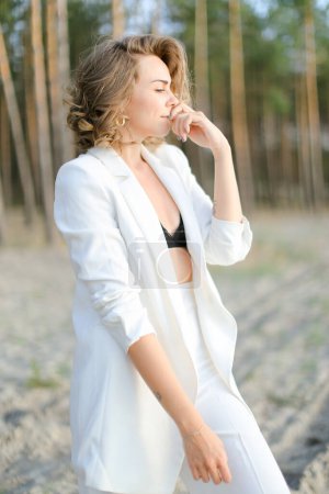 Photo for Blonde charming woman in white walking on sand beach and wearing white clothes. - Royalty Free Image