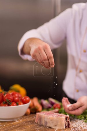 Foto de "Chef poniendo sal en jugosa rebanada de filete crudo
" - Imagen libre de derechos
