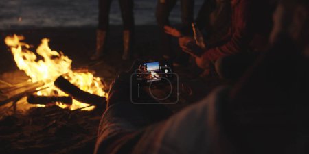 Foto de Pareja tomando fotos junto a la fogata en la playa - Imagen libre de derechos