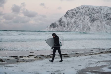 Téléchargez les photos : Surfeur arctique passant par la plage après le surf - en image libre de droit