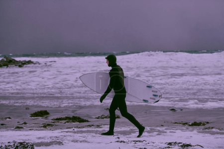 Téléchargez les photos : Surfeur arctique passant par la plage après le surf - en image libre de droit