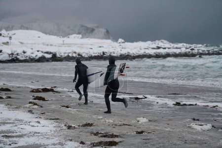 Téléchargez les photos : Surfeurs arctiques qui courent sur la plage après le surf - en image libre de droit