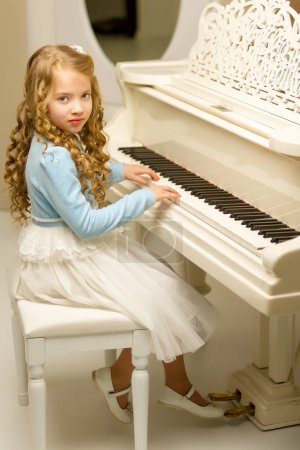 Téléchargez les photos : Belle petite fille joue sur un piano à queue blanc. - en image libre de droit