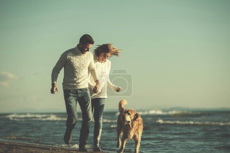 Téléchargez les photos : Couple avec chien s'amuser sur la plage le jour de l'autmun - en image libre de droit