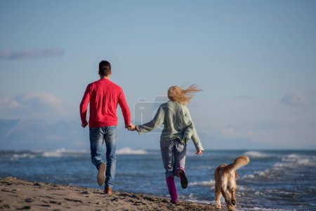 Téléchargez les photos : Couple avec chien s'amuser sur la plage le jour de l'autmun - en image libre de droit