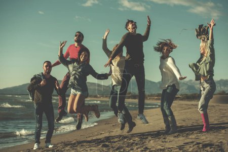 Téléchargez les photos : Jeunes amis sautant ensemble à la plage d'automne - en image libre de droit