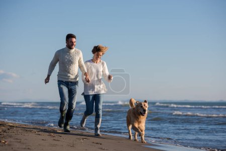 Foto de Pareja con perro divirtiéndose en la playa en día autmun - Imagen libre de derechos