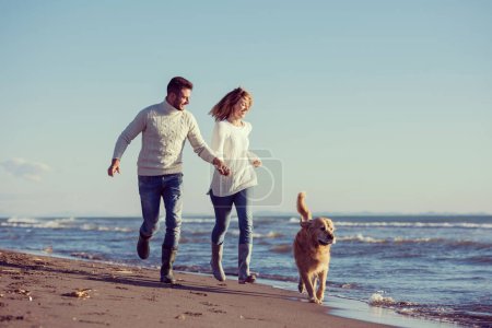 Photo for Couple with dog having fun on beach on autmun day - Royalty Free Image