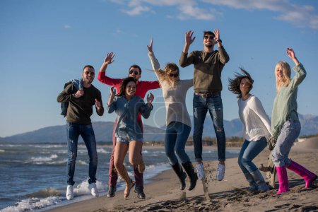 Foto de Jóvenes amigos saltando juntos en la playa de otoño - Imagen libre de derechos